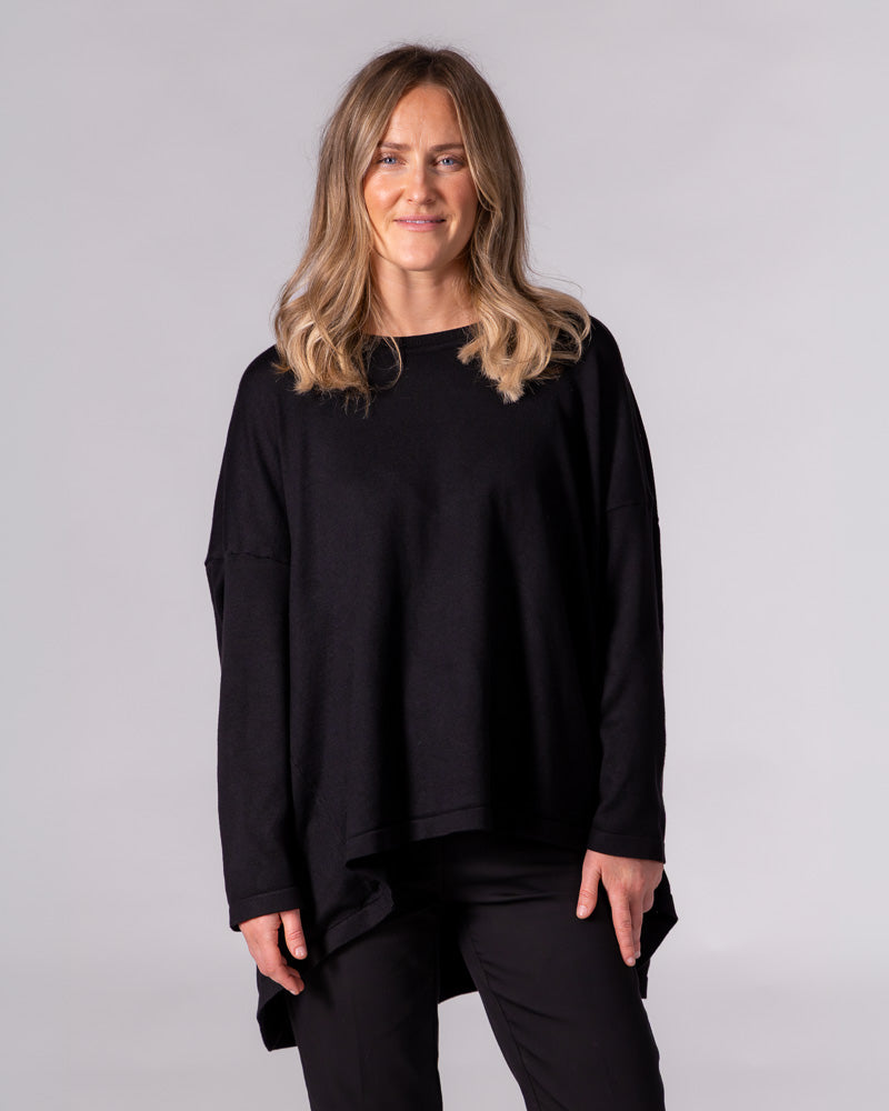 Black oversized crew neck knit jumper featuring dropped shoulders, fitted sleeves, and a draped high-low hem.