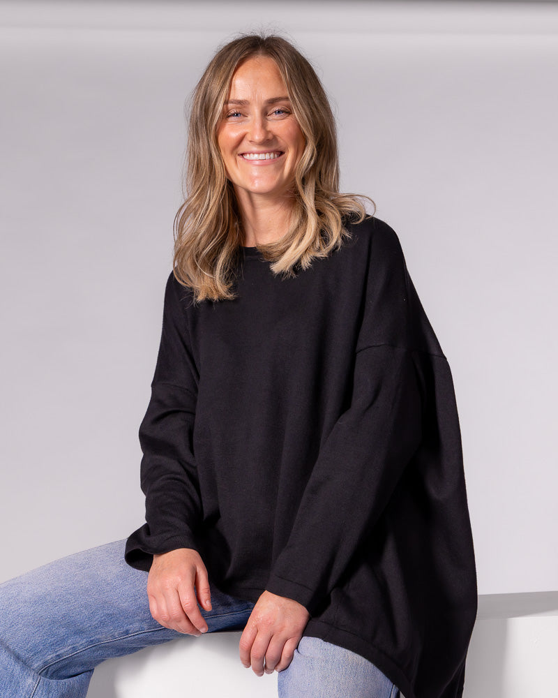 Oversized black cotton knit jumper featuring a crew neckline, dropped shoulders, and a fluid draped high-low hem.