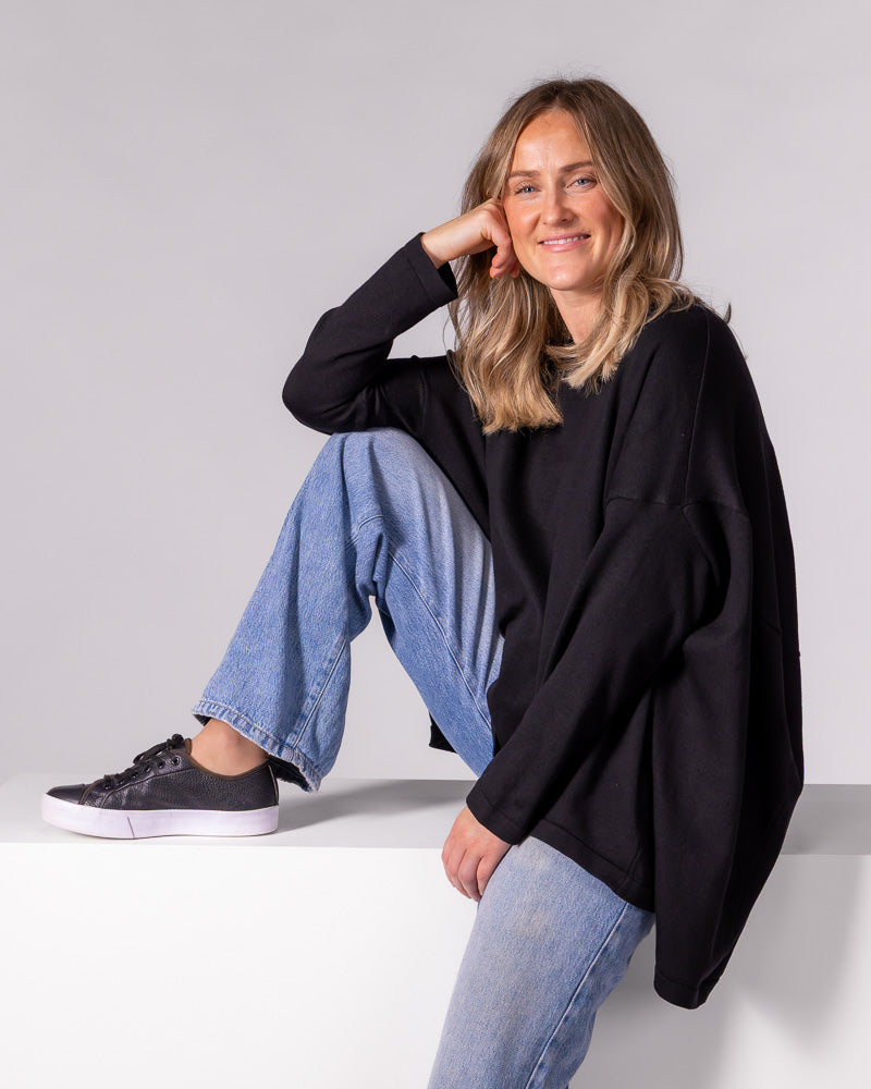 Black oversized cotton knit jumper featuring a crew neckline, long fitted sleeves, and a draped high-low hem.