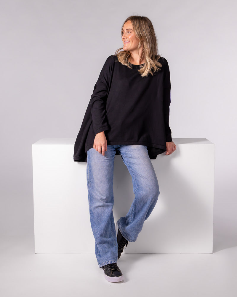 Black oversized knit jumper with a crew neckline, long fitted sleeves, and a draped high-low hem.