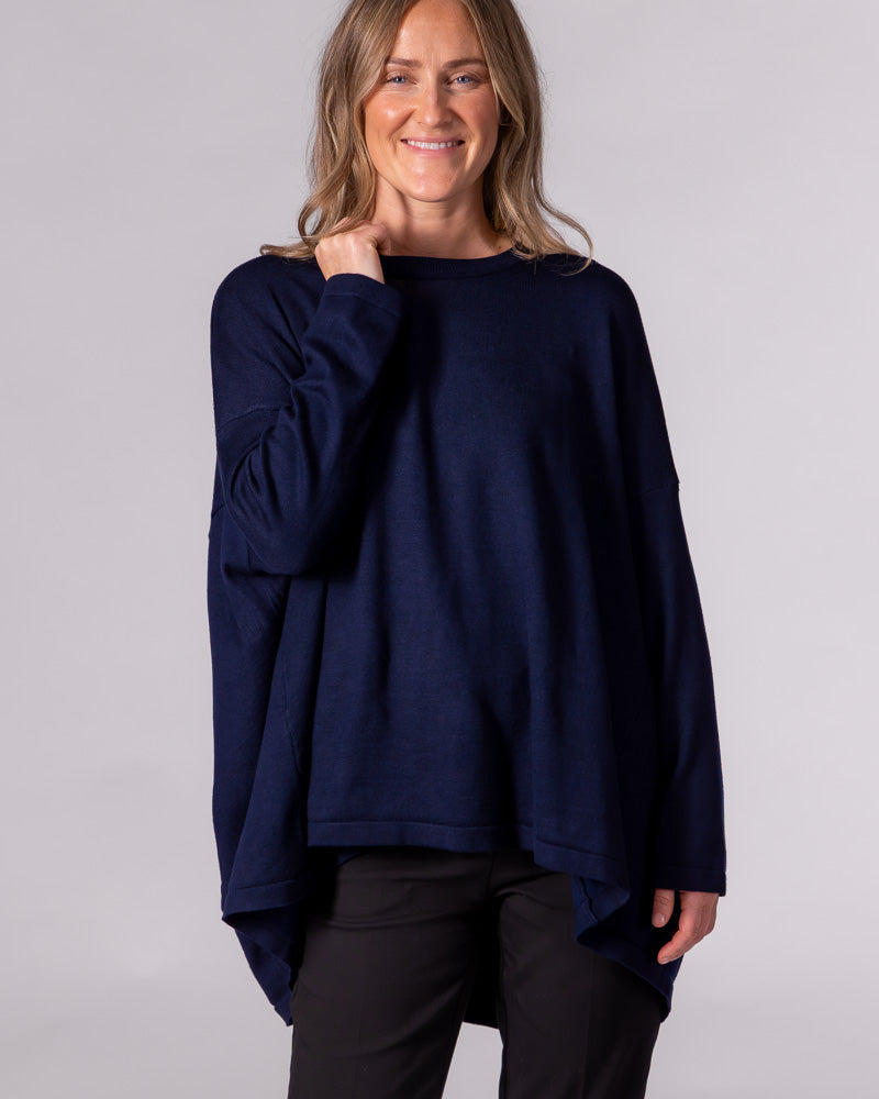 Oversized navy blue knit jumper featuring a crew neckline, dropped shoulders, and a draped high-low hem.