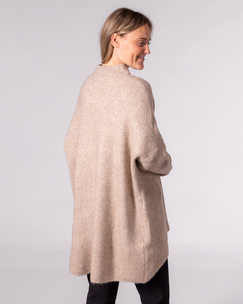 Back view of an oversized beige brushed knit jumper with a ribbed funnel neck, drop shoulders and a high-low hemline.