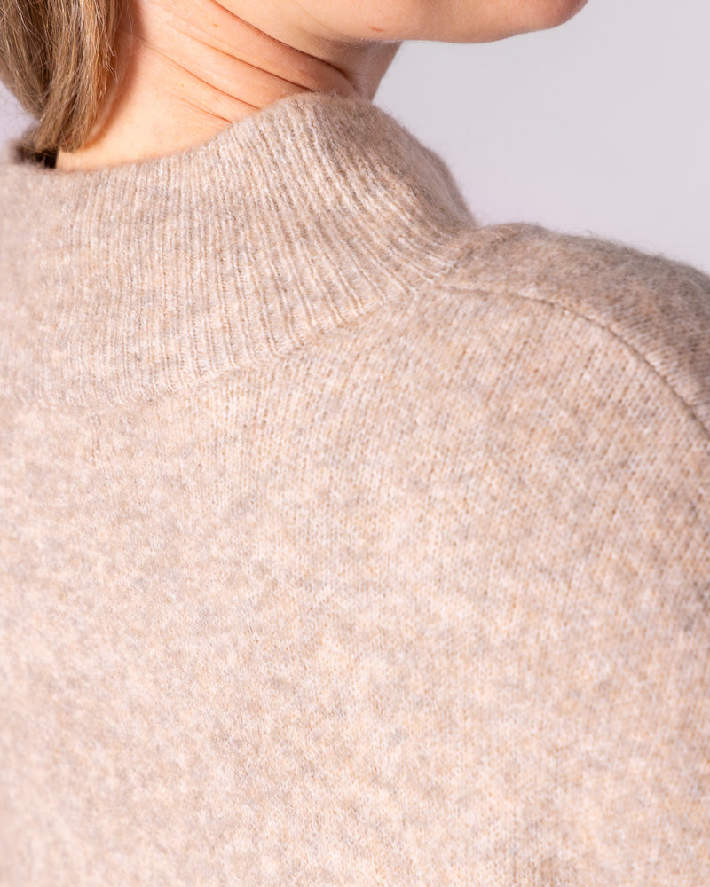 Close-up detailing the ribbed funnel neck and drop shoulder seam of a beige brushed knit jumper.