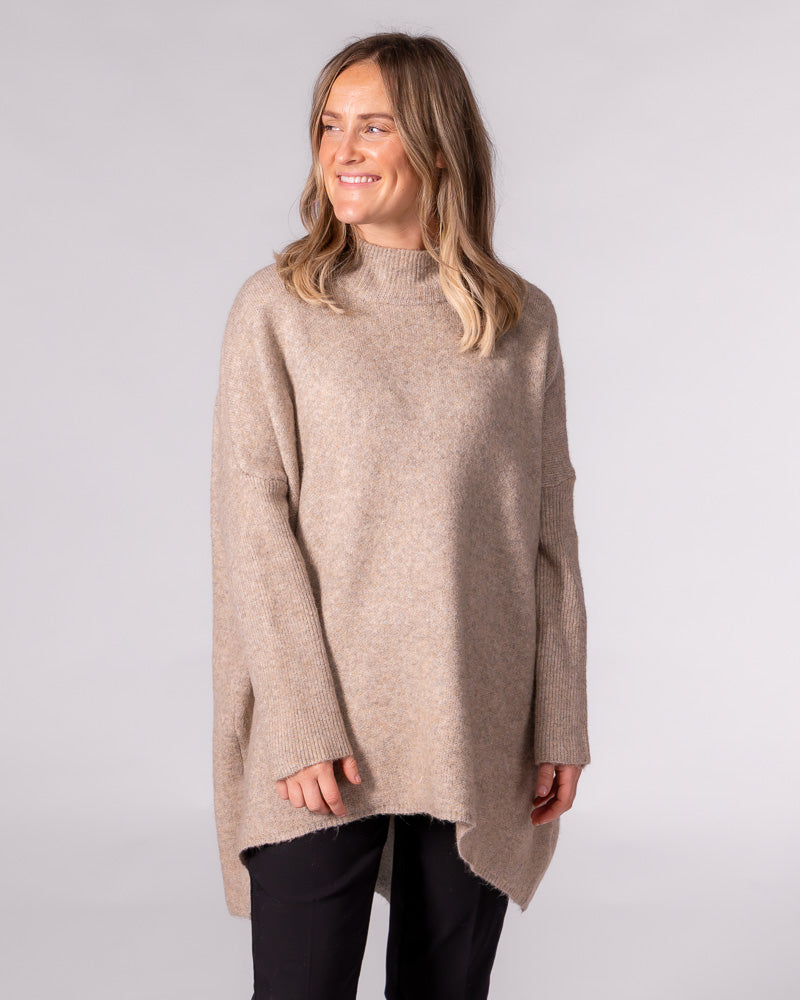Beige oversized brushed knit jumper featuring a ribbed funnel neck, drop shoulders, and a high-low hemline.