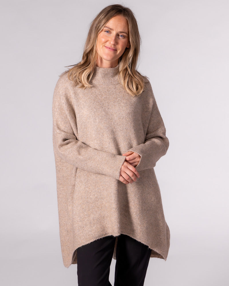 Oversized beige brushed knit jumper featuring a ribbed funnel neck, drop shoulders, and a distinct high-low hemline.