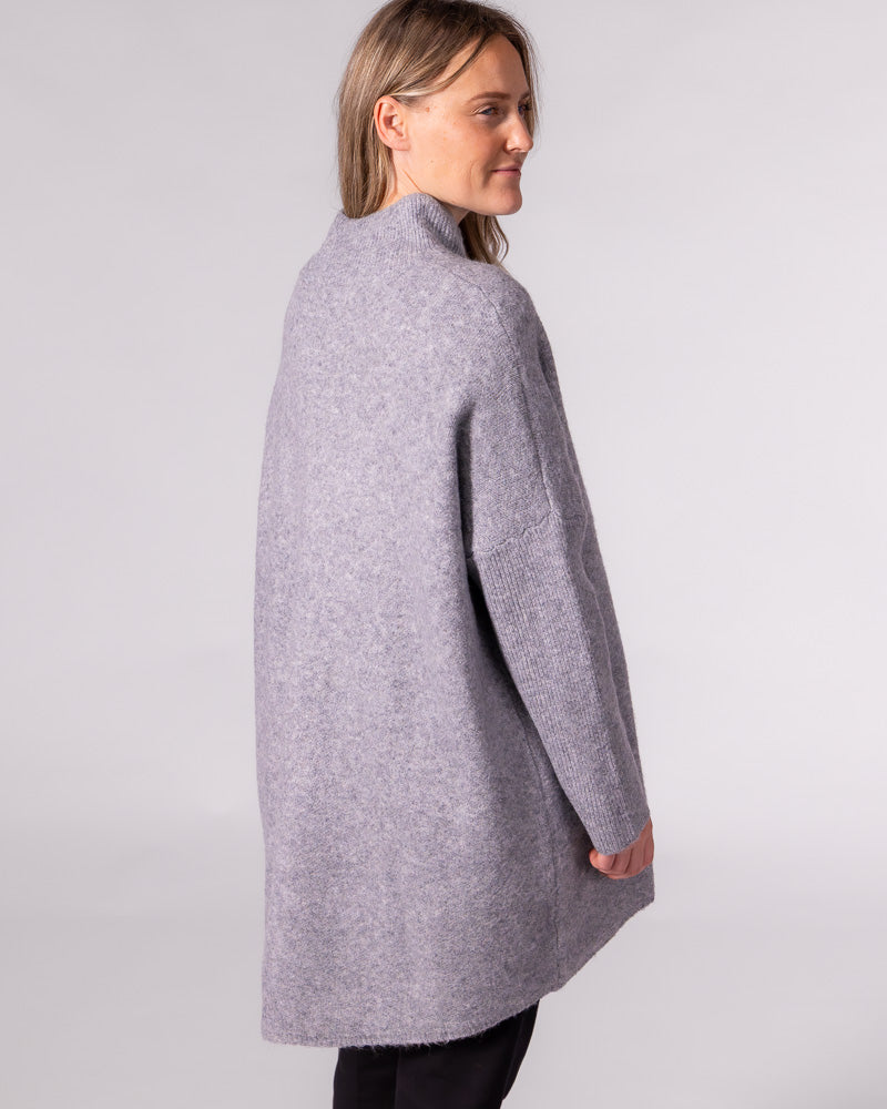 Oversized grey brushed knit jumper viewed from behind, showing drop shoulders, ribbed sleeves and a long back hem.