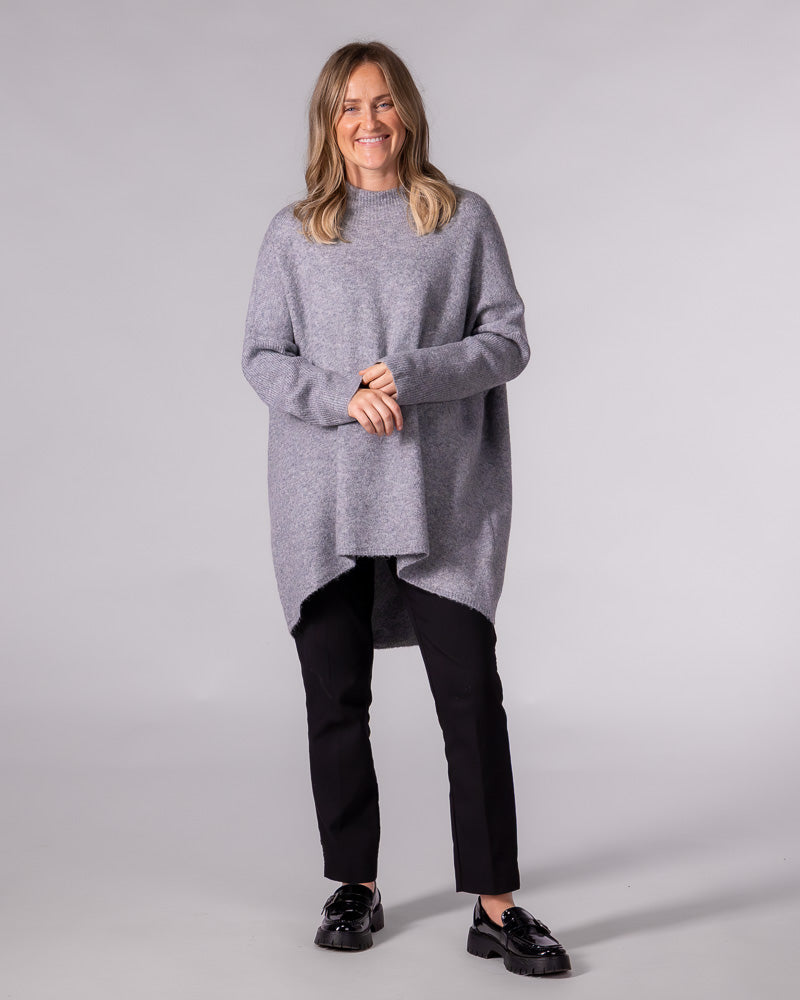 Grey oversized brushed knit jumper with a ribbed funnel neck, drop shoulders, and a prominent high-low hemline.