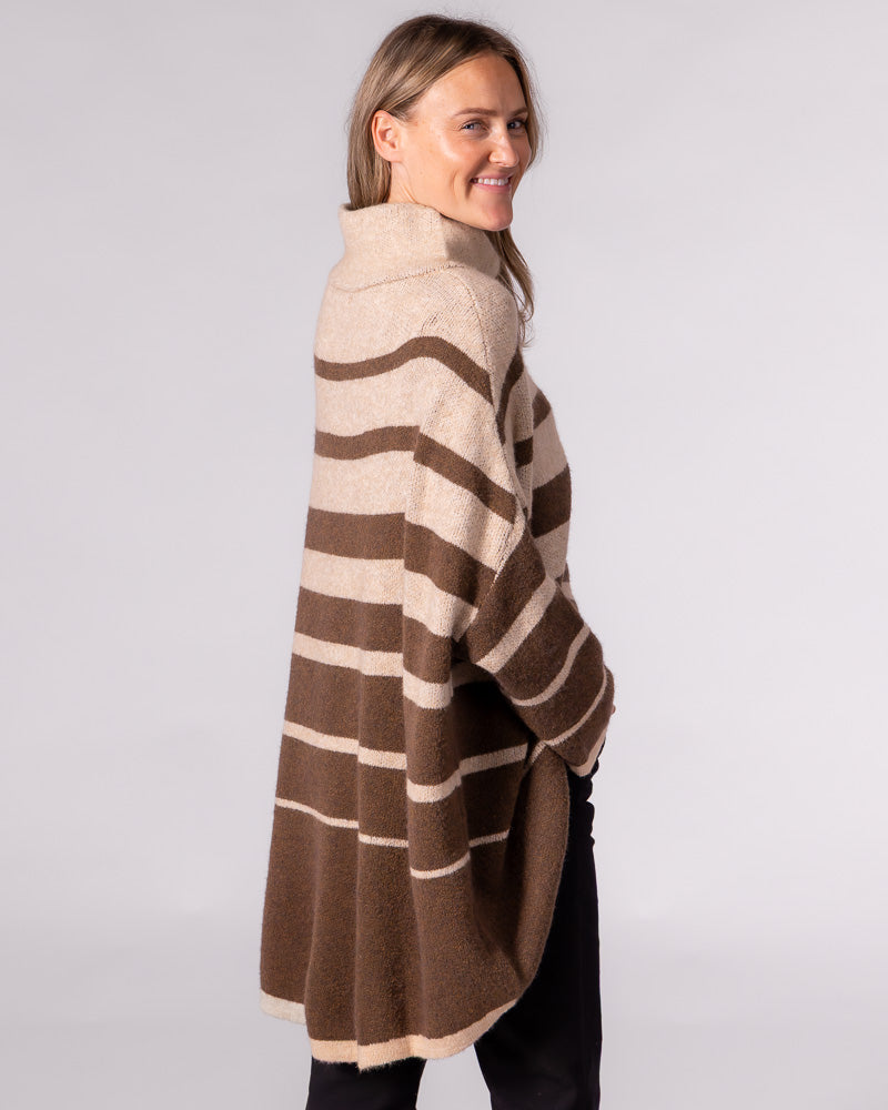 Side view of an oversized brown striped brushed knit jumper featuring a funnel neck, drop shoulders, and a high-low hem.
