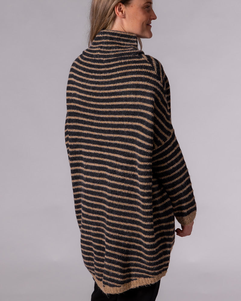 Back view of a black and mocha striped oversized knit jumper with a funnel neck, drop shoulders, and long scooped hem.