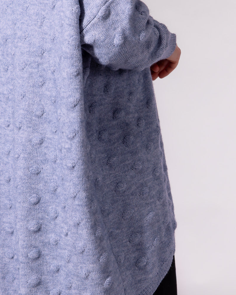Close-up side view of a light blue oversized jumper highlighting its raised bubble knit texture and curved scooped hem.
