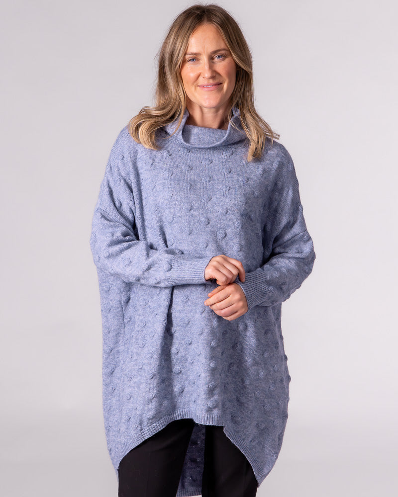 Oversized light blue knit jumper featuring a funnel neck, textured bubble pattern, and a high-low scooped hem.