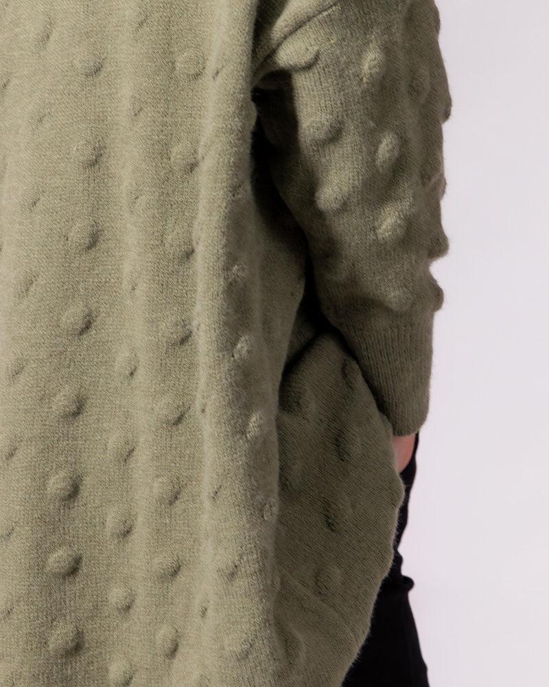 Olive green bubble knit jumper showcasing a distinctive raised texture, draped oversized fit and ribbed sleeve cuff.