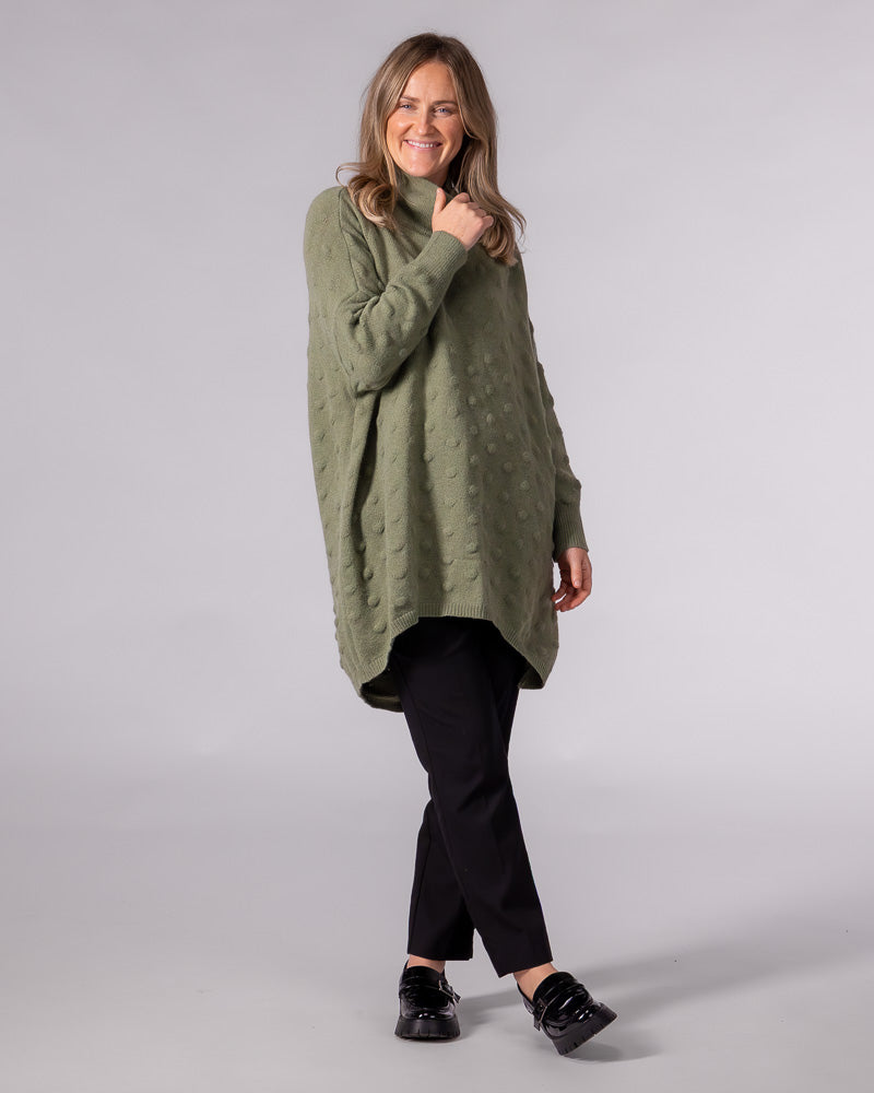 Oversized olive knit jumper with a raised bubble texture, funnel neck, and a scooped high-low hemline.