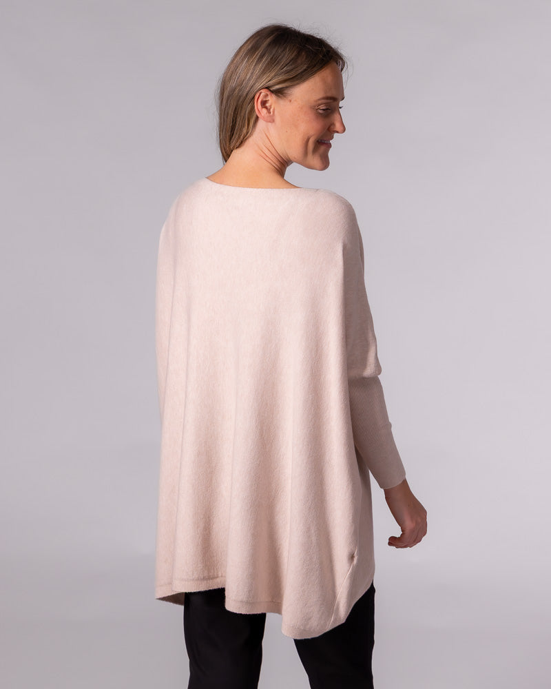 Oversized blush cotton jumper featuring a draped back silhouette, drop shoulders, and long fitted sleeves.