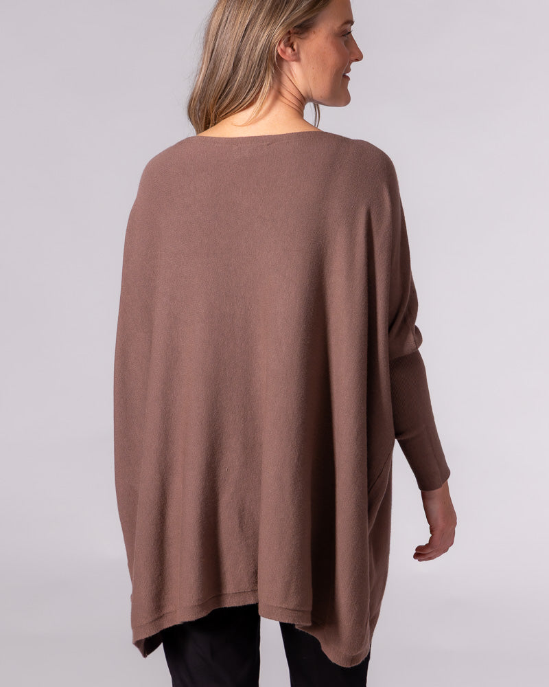Back view of the oversized brown cotton jumper showcasing its draped design, drop shoulders, and fitted ribbed sleeves.