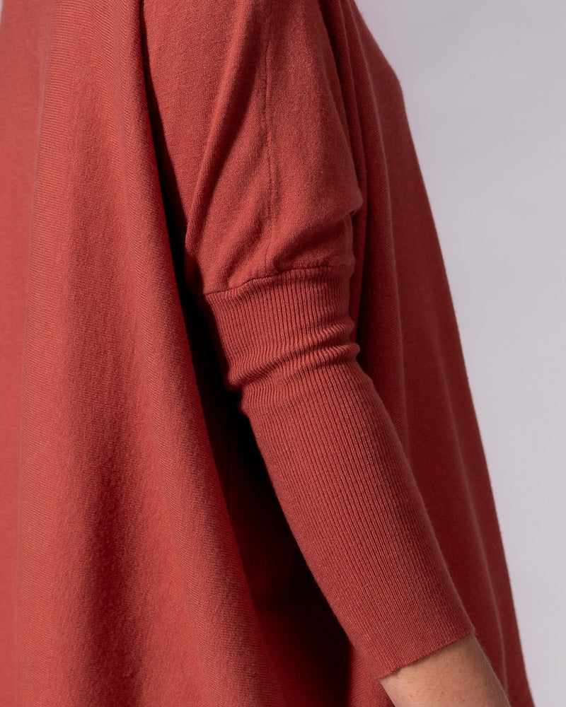 Burnt orange cotton jumper showing a drop shoulder, long ribbed fitted sleeve, and an oversized draped silhouette.