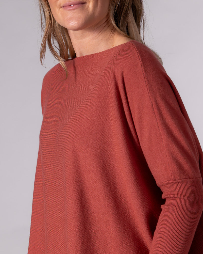 Burnt orange cotton knit jumper displaying a wide boat neckline, relaxed drop shoulder, and tightly ribbed lower sleeve.