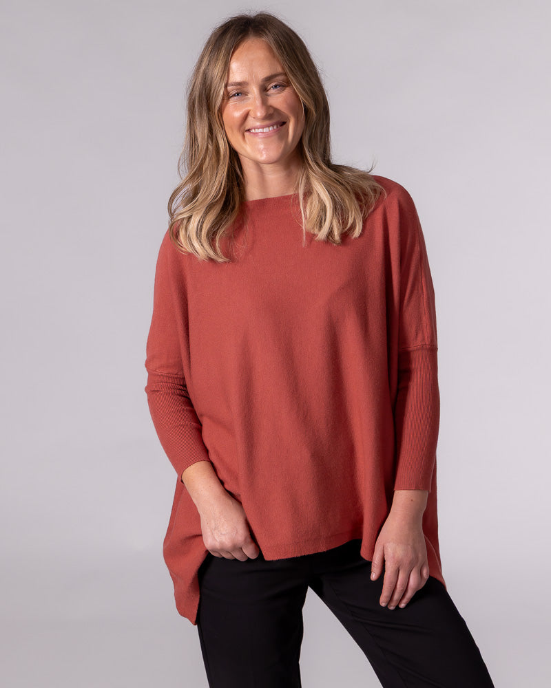 Oversized burnt orange cotton knit jumper featuring a wide boat neckline, drop shoulders, and fitted ribbed sleeves.