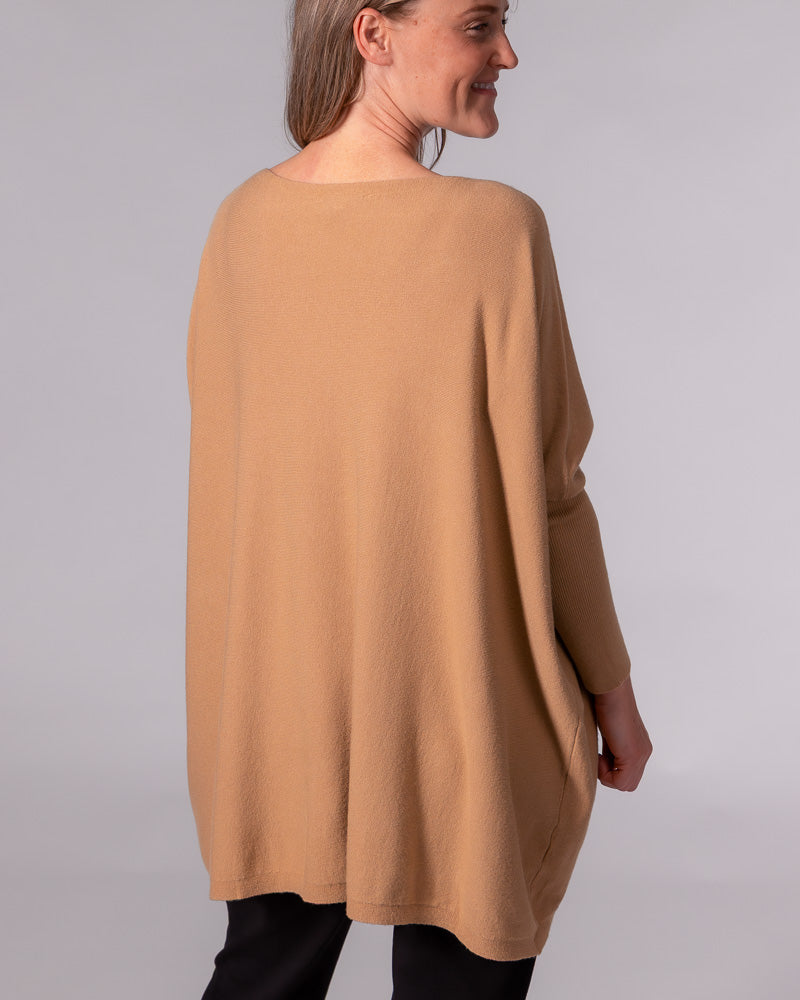 Back view of an oversized camel cotton knit jumper featuring a draped silhouette, hi-low hem, and long fitted sleeves.
