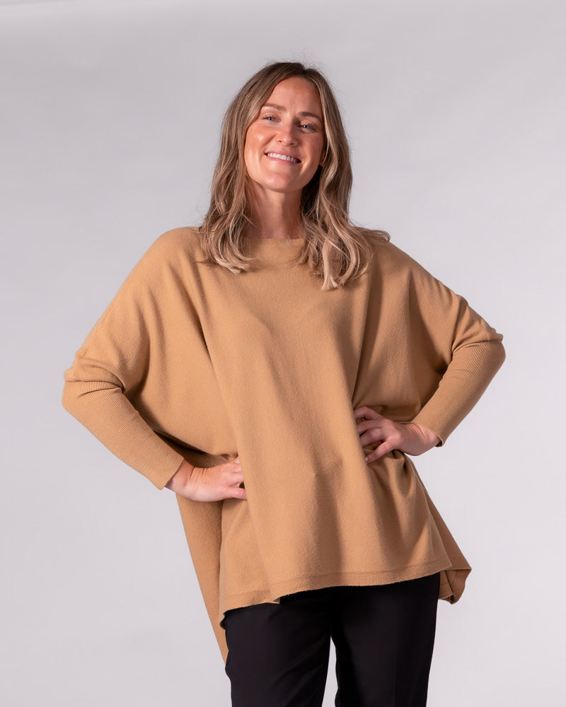 Oversized camel cotton knit jumper displaying a wide boat neckline, fitted drop sleeves, and a draped hi-low hem.