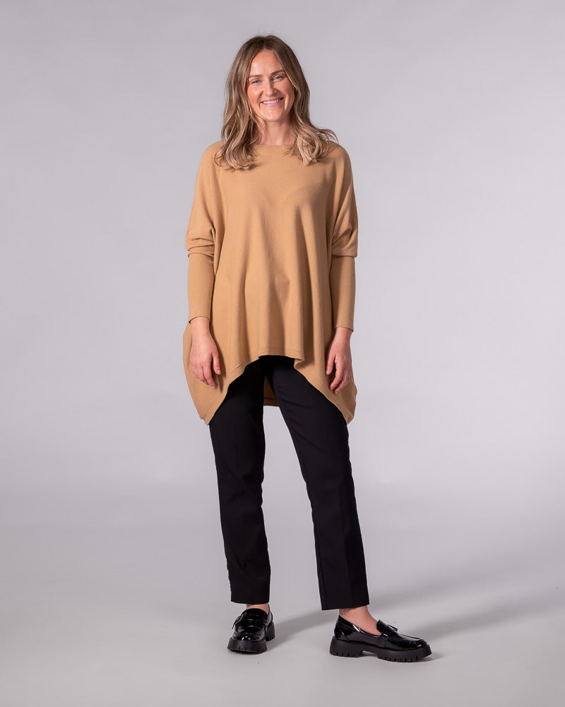 Oversized camel cotton jumper showcasing a boat neckline, drop shoulders, fitted sleeves, and a draped hi-low hem.