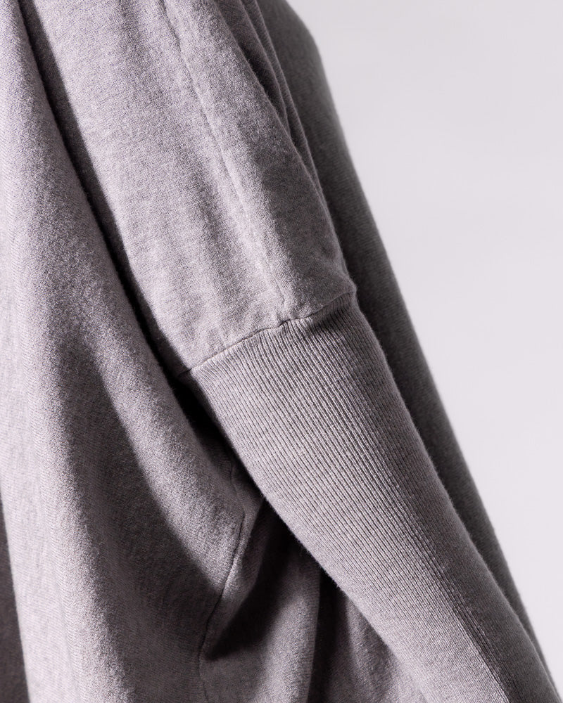 Close-up of the grey knit top, displaying the contrast between the long fitted ribbed sleeve and loose body.