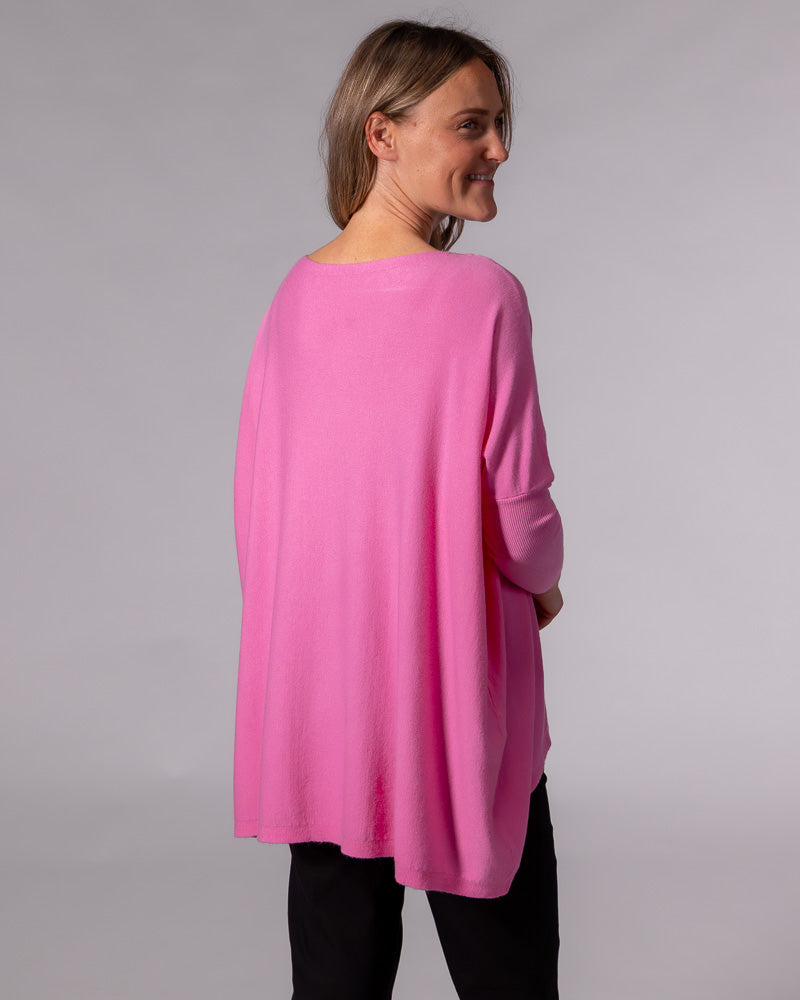 Oversized hot pink cotton knit jumper showing a draped back design, drop shoulders, and fitted sleeves.