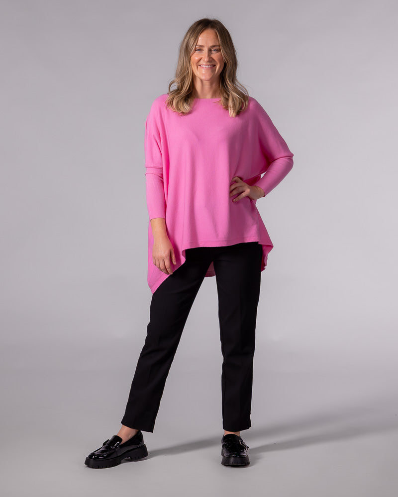 Hot pink oversized cotton knit jumper with a wide boat neckline, drop shoulders, fitted sleeves, and a draped hi-low hem.