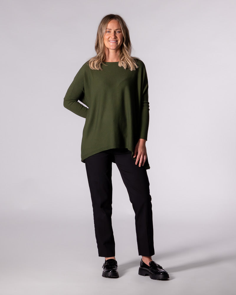 Full-length styling of the khaki Karma Kameleon knit top paired with black pants and chunky black loafers.