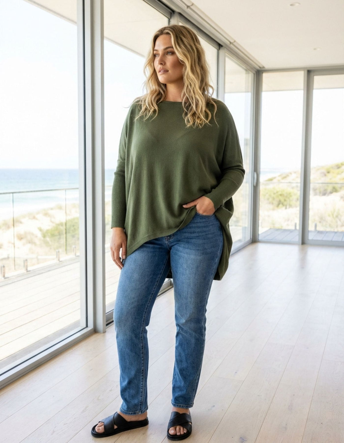 Full-length styling of the oversized khaki cotton jumper paired with blue denim jeans and black slide sandals.
