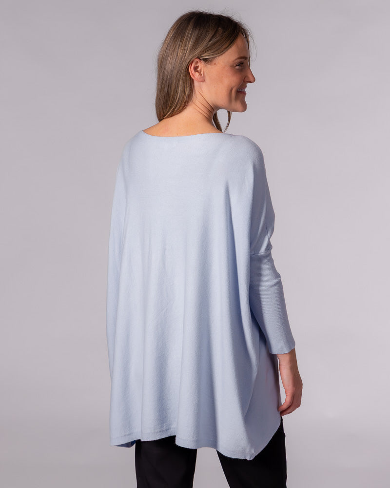 Back view of the light blue cotton knit jumper showing the oversized draped back, drop shoulders and long fitted sleeves.