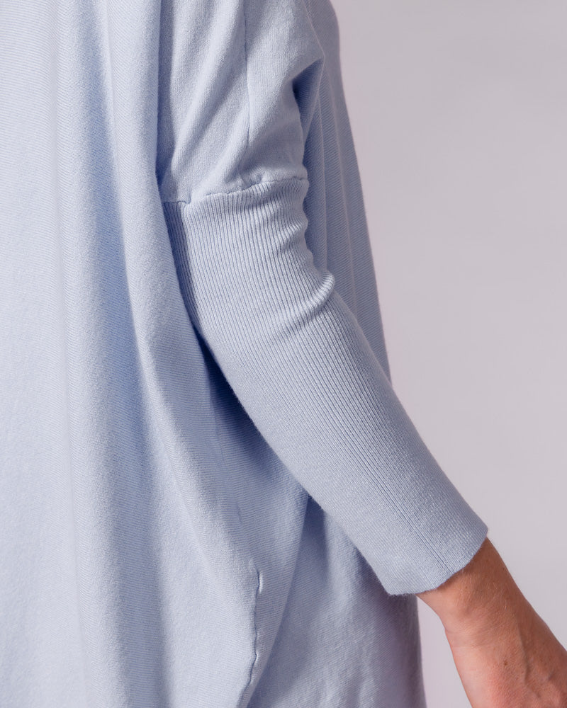 Light blue cotton jumper highlighting a drop shoulder seam and fitted ribbed sleeve next to an oversized draped body.