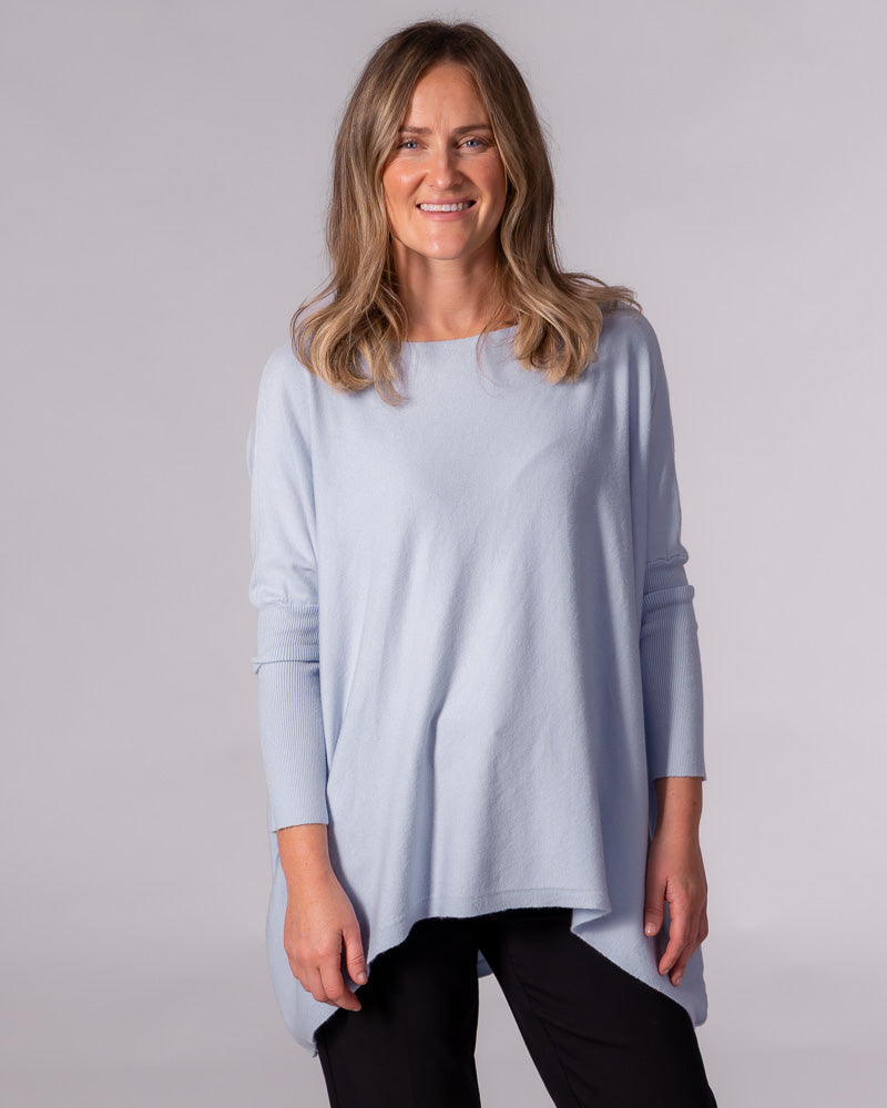 Light blue oversized cotton knit jumper with a wide boat neckline, fitted ribbed sleeves, and a draped hi-low hem.