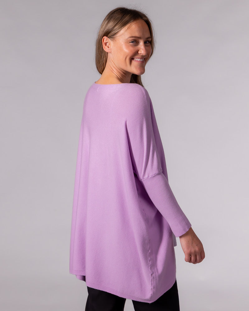 Back of the oversized lilac cotton jumper showing its draped silhouette, drop shoulders, and fitted ribbed sleeves.