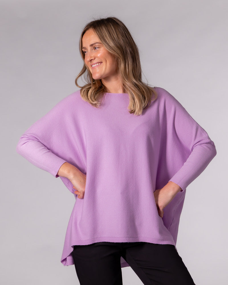 Oversized lilac cotton knit jumper with a wide boat neckline, drop shoulders, fitted sleeves, and a hi-low hem.