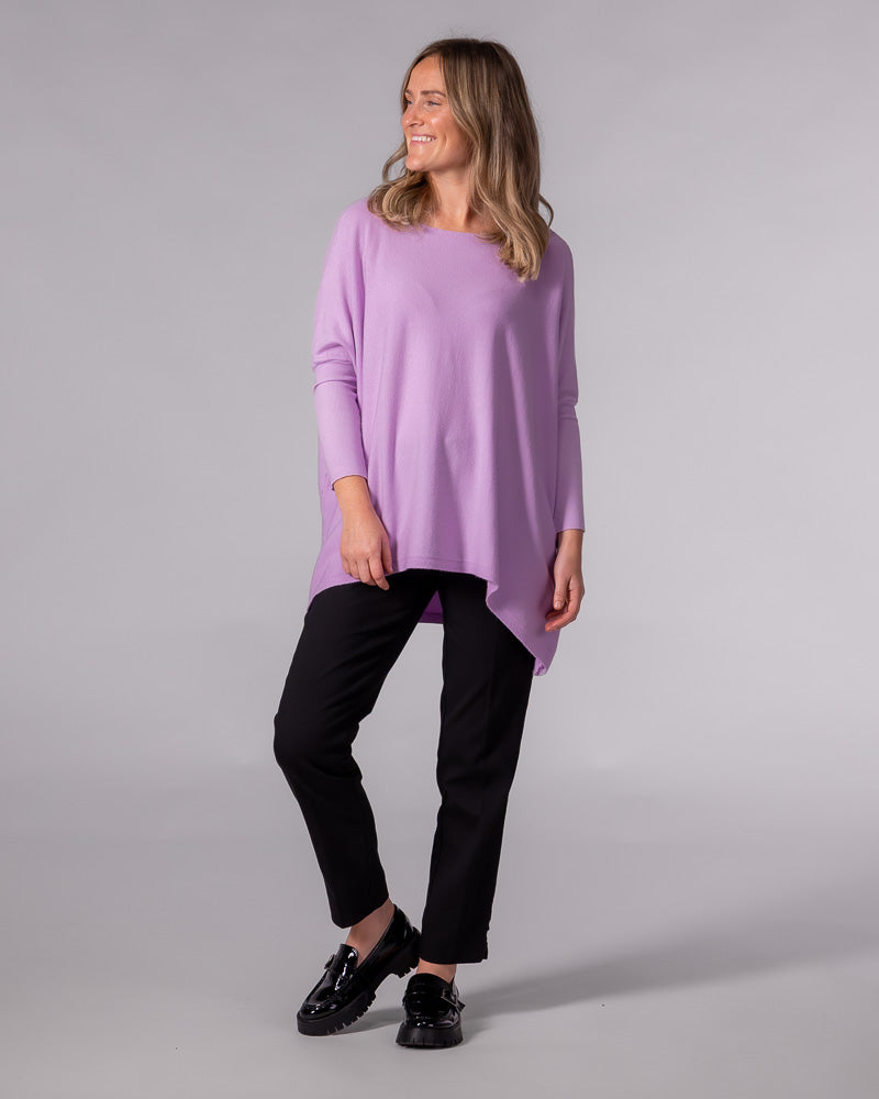Oversized lilac cotton knit jumper with a wide boat neckline, drop shoulders, fitted sleeves, and a draped hi-low hem.