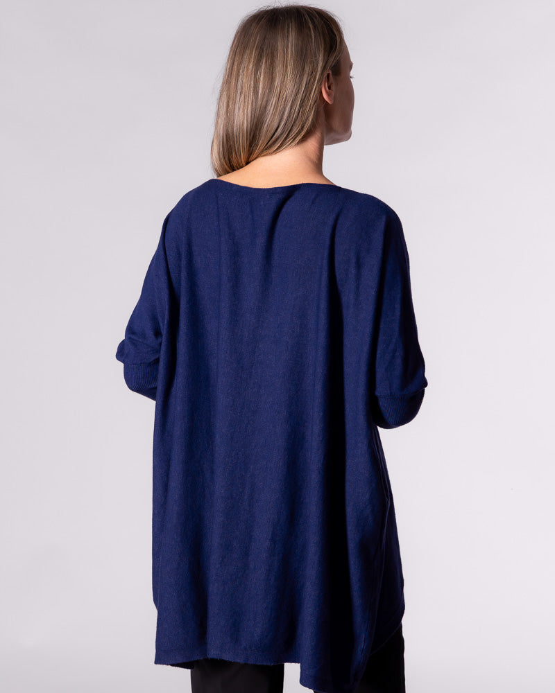 Mid-length back view. Model is facing away, looking slightly to the right, showing the full length of the back hemline dropping down.