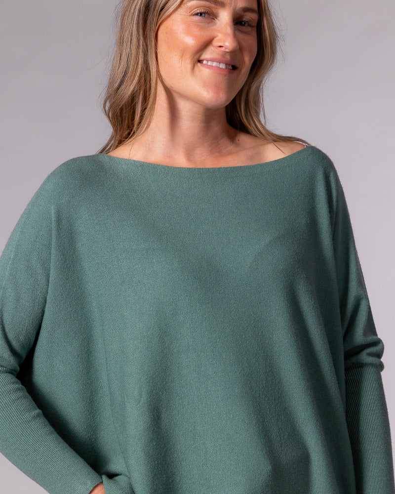 Sage green cotton knit jumper featuring a wide boat neckline, draped oversized fit, and fitted ribbed sleeves.