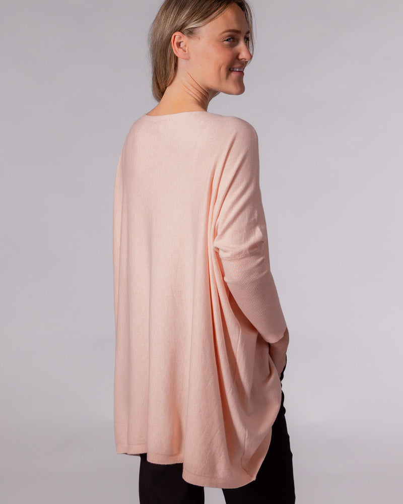 Soft pink cotton knit jumper showing a draped back design, relaxed drop shoulders, and fitted lower sleeves.