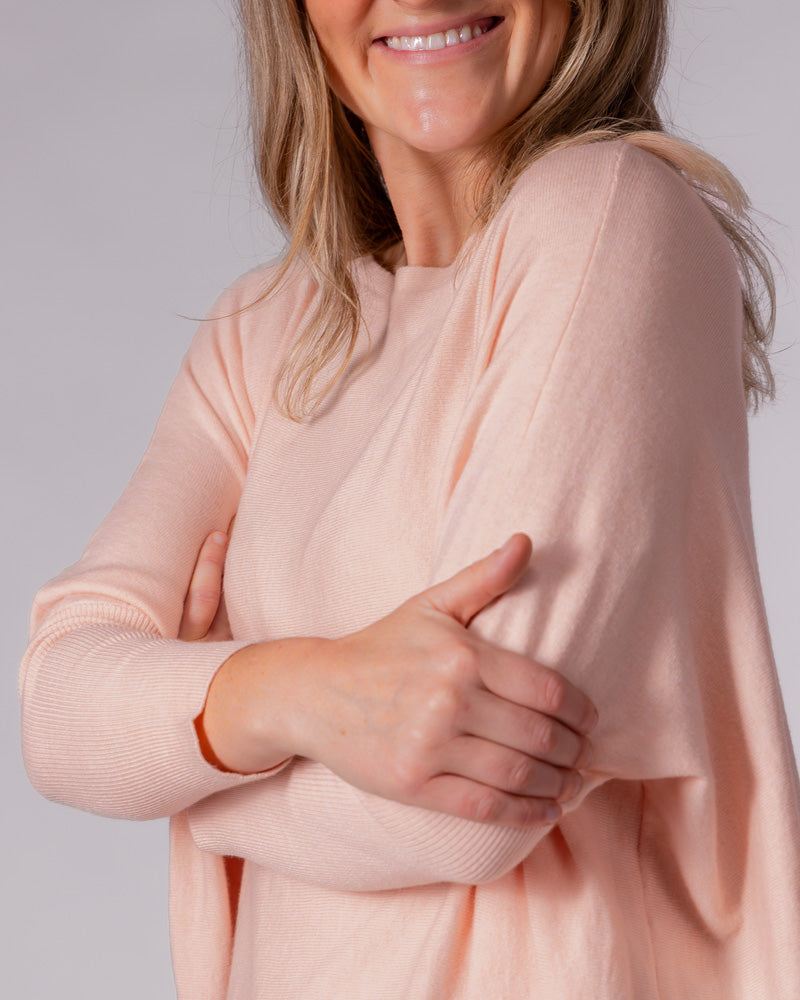 Soft pink oversized cotton jumper featuring a wide neckline, relaxed draped body, and fitted ribbed sleeves.