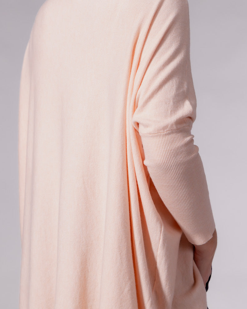 Soft pink cotton jumper displaying the oversized draped back, drop shoulder, and fitted ribbed sleeve.