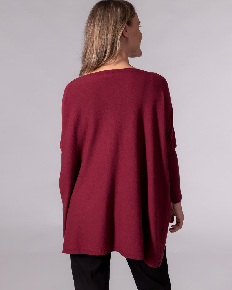 Back view of the wine red cotton knit jumper showing an oversized draped silhouette, drop shoulders and fitted sleeves.