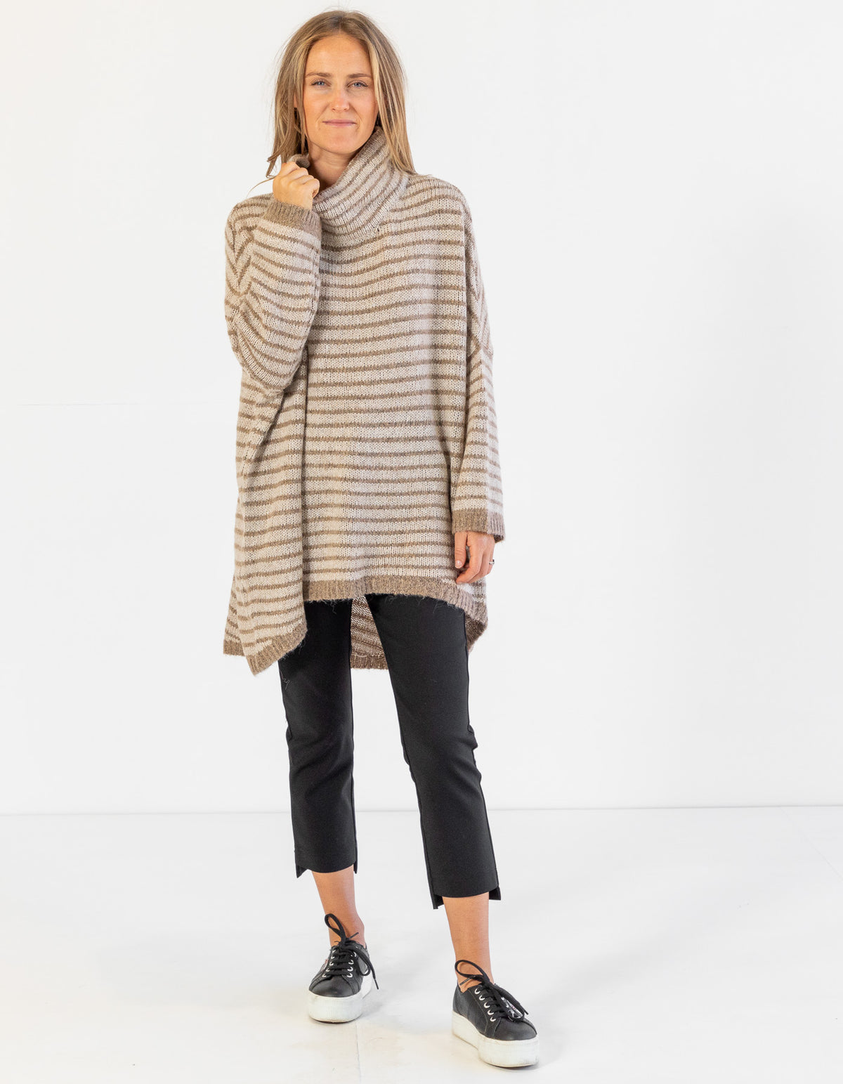 Full-length view of the beige and mocha stripe jumper styled with black pants and sneakers.