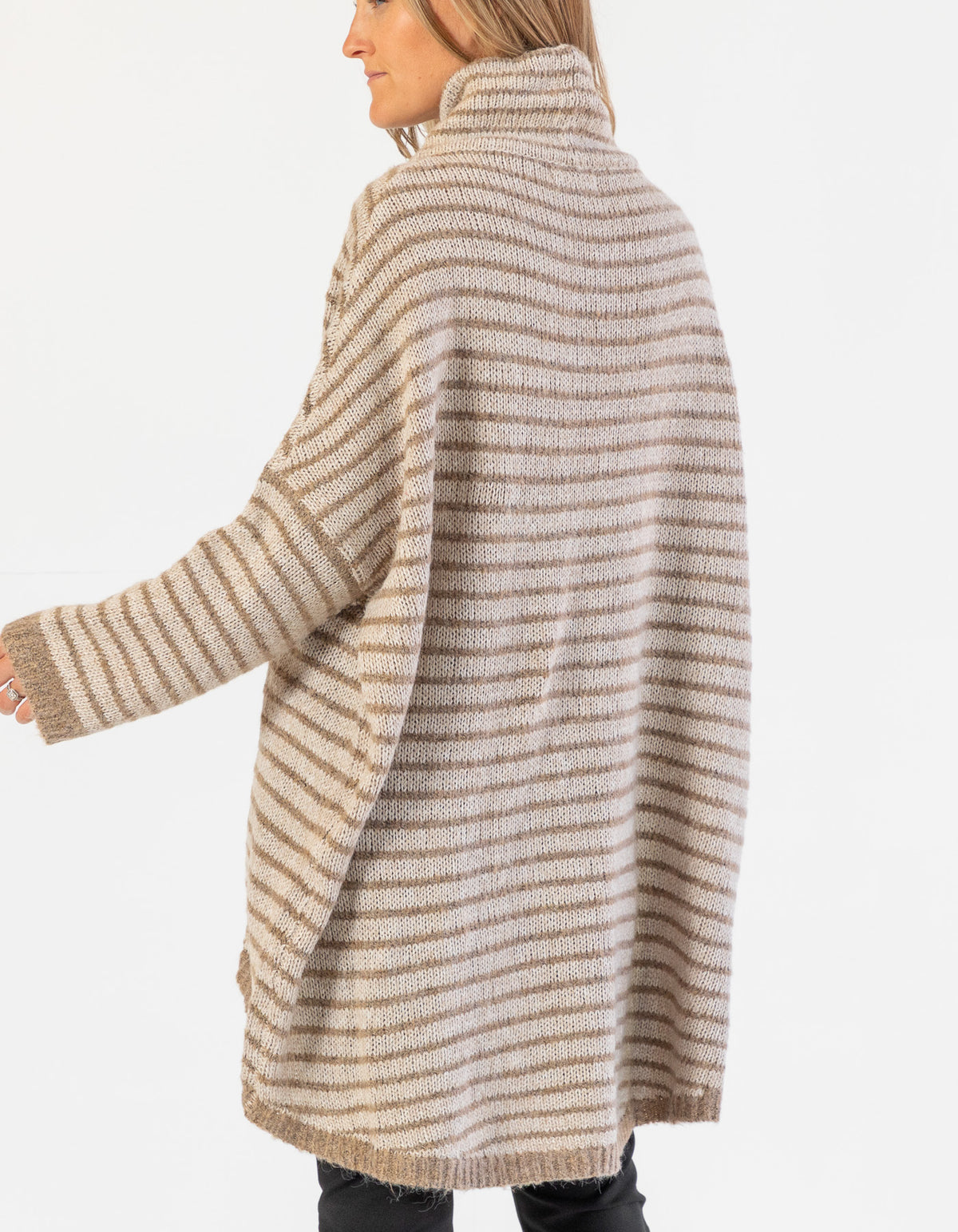 Rear half-body shot showing the extended back drape of the beige and mocha stripe jumper over black pants.