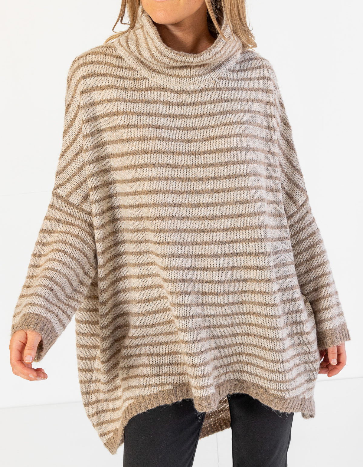 Front half-body shot of the oversized beige and mocha stripe knitwear paired with black pants.