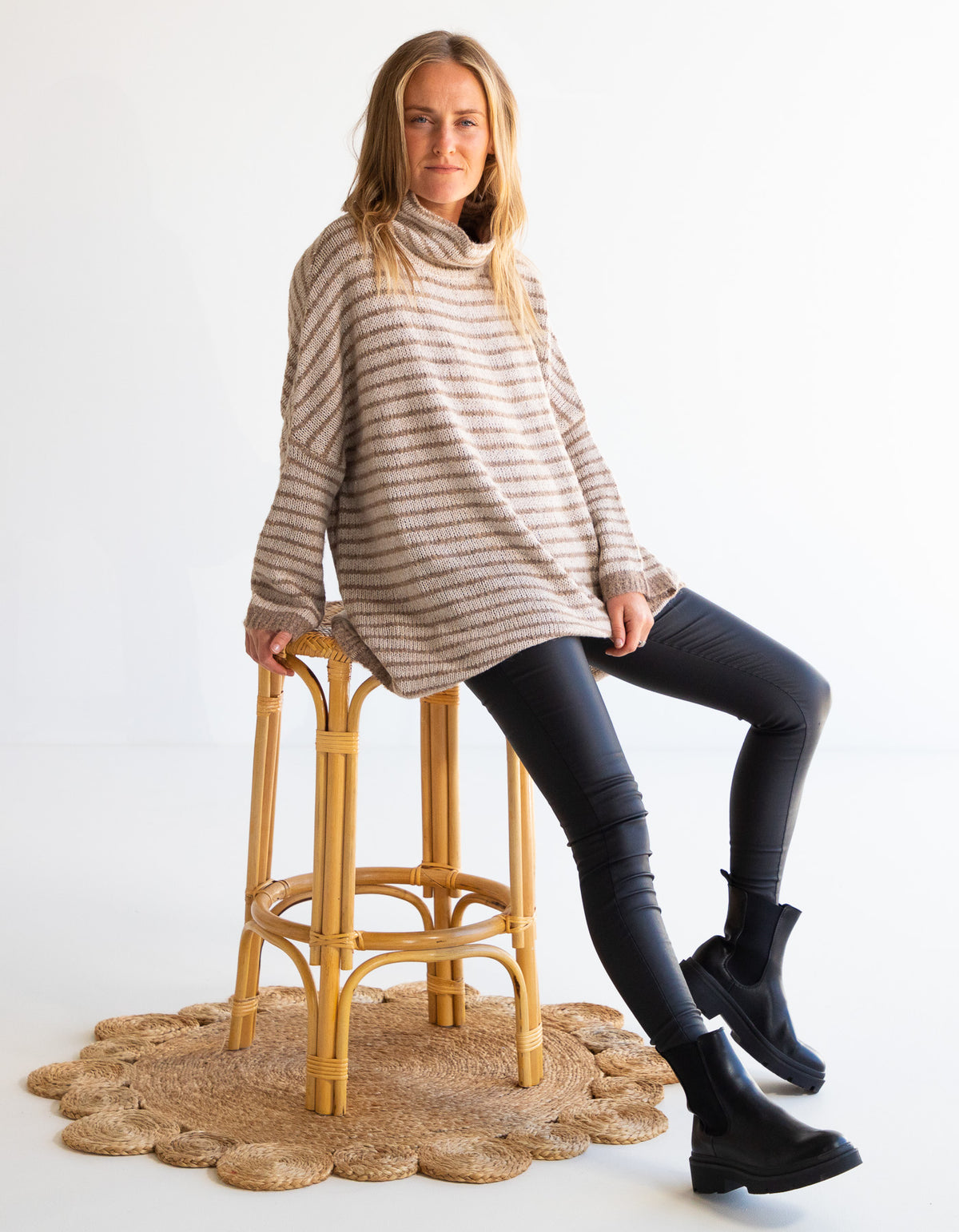 Full-body shot of the Karma Kameleon beige and mocha stripe knit top paired with black pants and boots.